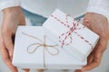 Young caucasian woman in jeans shirt holds in hands stacked gift boxes wrapped in white paper tied with striped twine. Christmas