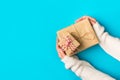 Woman in knitted white sweater holds in hand stack of gift boxes wrapped in brown Kraft paper on blue. Christmas New Years