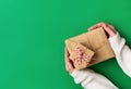 Young caucasian woman in knitted white sweater holds in hand stack of gift boxes wrapped in brown Kraft paper on green background