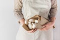 Young Caucasian woman in linen apron holds in hands brown paper bag with freshly picked white button mushrooms in kitchen