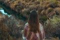 Young caucasian woman with long chestnut hair in checkered wool plaid looks at river standing in field meadow. Cozy autumn Royalty Free Stock Photo