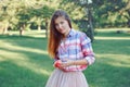 Young Caucasian woman with long red hair in plaid shirt posing in park