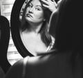 Young Caucasian woman looking at herself in vanity mirror checking her hair and makeup, grayscale Royalty Free Stock Photo