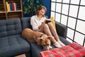 Young caucasian woman looking photo sitting on sofa with dog at home