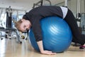 Young caucasian woman lying on blue gymnastic ball looking exhausted, tired, bored and weary at the gym