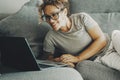 Young Caucasian woman lying on couch in living room work online on laptop gadget. Millennial female relax rest on sofa at home Royalty Free Stock Photo