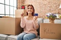 Young caucasian woman moving to a new home holding credit card smiling happy pointing with hand and finger to the side Royalty Free Stock Photo