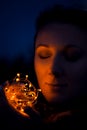 Young caucasian woman outside in the evening holding christmas lights in her hands with her eyes closed and smiling thinking about Royalty Free Stock Photo