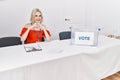 Young caucasian woman at political election sitting by ballot smiling in love showing heart symbol and shape with hands