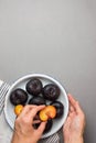 Young caucasian woman puts halved dark red purple plums with bright yellow reddish flesh on white plate. Rustic Style. Autumn