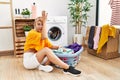 Young caucasian woman putting dirty laundry into washing machine surprised with hand on head for mistake, remember error