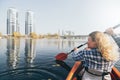 Young woman in red kayak rowing towards modern buildings on the waters of Dnipro river in Kyiv, Ukraine