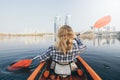 Young woman in red kayak rowing towards modern buildings on the waters of Dnipro river in Kyiv, Ukraine