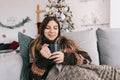 Young caucasian woman relaxing on a sofa at home and holding mug with hot drink in Christmas holidays Royalty Free Stock Photo