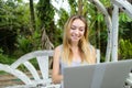 Young caucasian woman resting on swing and using laptop, palms in background. Royalty Free Stock Photo