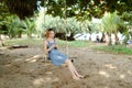 Young caucasian woman riding swing and using smatrphone, sand and tree in background. Royalty Free Stock Photo