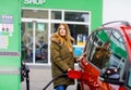 Young caucasian woman at self-service gas station, hold fuel nozzle and refuel the car with petrol, diesel, gas. Pretty Royalty Free Stock Photo