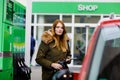 Young caucasian woman at self-service gas station, hold fuel nozzle and refuel the car with petrol, diesel, gas. Pretty Royalty Free Stock Photo