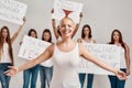 Young caucasian woman with shaved head in white shirt looking excited. Group of diverse women holding protest banners Royalty Free Stock Photo