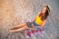 Young caucasian woman in shorts and a straw hat uses her laptop while sitting on the sandy beach by the sea at sunset Royalty Free Stock Photo