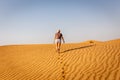 Young caucasian woman in shorts and t-shirt going away towards the arabian desert dunes, footprints and ripples in the sand.