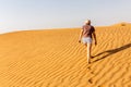 Young caucasian woman in shorts and t-shirt walking alone on a sand dune towards the arabian desert, footprints and ripples in the Royalty Free Stock Photo