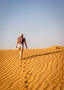 Young caucasian woman in shorts and t-shirt walking alone on a sand dune towards the arabian desert, UAE