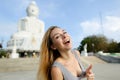 Young caucasian woman showing thumbs up, white Buddha statue in Phuket in background.