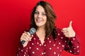 Young caucasian woman singing song using microphone smiling happy and positive, thumb up doing excellent and approval sign Royalty Free Stock Photo