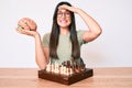 Young caucasian woman sitting at the desk playing chess holding brain stressed and frustrated with hand on head, surprised and Royalty Free Stock Photo