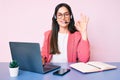 Young caucasian woman sitting at the desk wearing call center agent headset working using laptop doing ok sign with fingers, Royalty Free Stock Photo