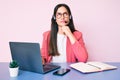 Young caucasian woman sitting at the desk wearing call center agent headset working using laptop serious face thinking about Royalty Free Stock Photo