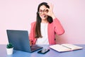 Young caucasian woman sitting at the desk wearing call center agent headset working using laptop smiling happy doing ok sign with Royalty Free Stock Photo