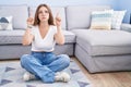 Young caucasian woman sitting on the floor at the living room pointing up looking sad and upset, indicating direction with Royalty Free Stock Photo