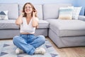 Young caucasian woman sitting on the floor at the living room smiling pulling ears with fingers, funny gesture Royalty Free Stock Photo