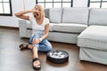 Young caucasian woman sitting at home by vacuum robot peeking in shock covering face and eyes with hand, looking through fingers