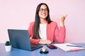 Young caucasian woman sitting at the recepcionist desk working using laptop smiling with happy face looking and pointing to the