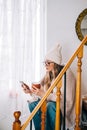 Young caucasian woman sitting on a stairs at home, drinking tea and using mobile phone Royalty Free Stock Photo