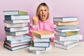 Young caucasian woman sitting on the table with books angry and mad raising fist frustrated and furious while shouting with anger Royalty Free Stock Photo
