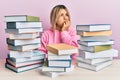 Young caucasian woman sitting on the table with books looking stressed and nervous with hands on mouth biting nails