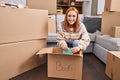 Young caucasian woman smiling confident unpacking books cardboard box at new home Royalty Free Stock Photo