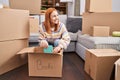 Young caucasian woman smiling confident unpacking books cardboard box at new home Royalty Free Stock Photo