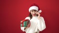 Young caucasian woman smiling wearing christmas hat holding gift speaking on the phone over isolated red background Royalty Free Stock Photo