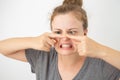 Young caucasian woman squeezing a pimple on her nose, funny facial expression