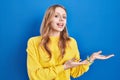 Young caucasian woman standing over blue background pointing aside with hands open palms showing copy space, presenting Royalty Free Stock Photo
