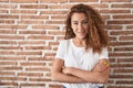 Young caucasian woman standing over bricks wall background happy face smiling with crossed arms looking at the camera Royalty Free Stock Photo