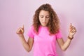 Young caucasian woman standing over pink background pointing down looking sad and upset, indicating direction with fingers, Royalty Free Stock Photo