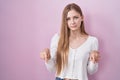 Young caucasian woman standing over pink background pointing down looking sad and upset, indicating direction with fingers, Royalty Free Stock Photo