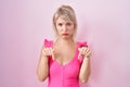 Young caucasian woman standing over pink background pointing down looking sad and upset, indicating direction with fingers, Royalty Free Stock Photo