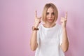 Young caucasian woman standing over pink background pointing up looking sad and upset, indicating direction with fingers, unhappy Royalty Free Stock Photo